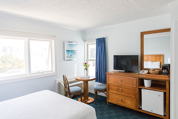 A hotel room with a bed, table, TV, and mini fridge.