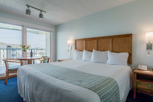 A hotel room with a large bed, balcony, and small table.